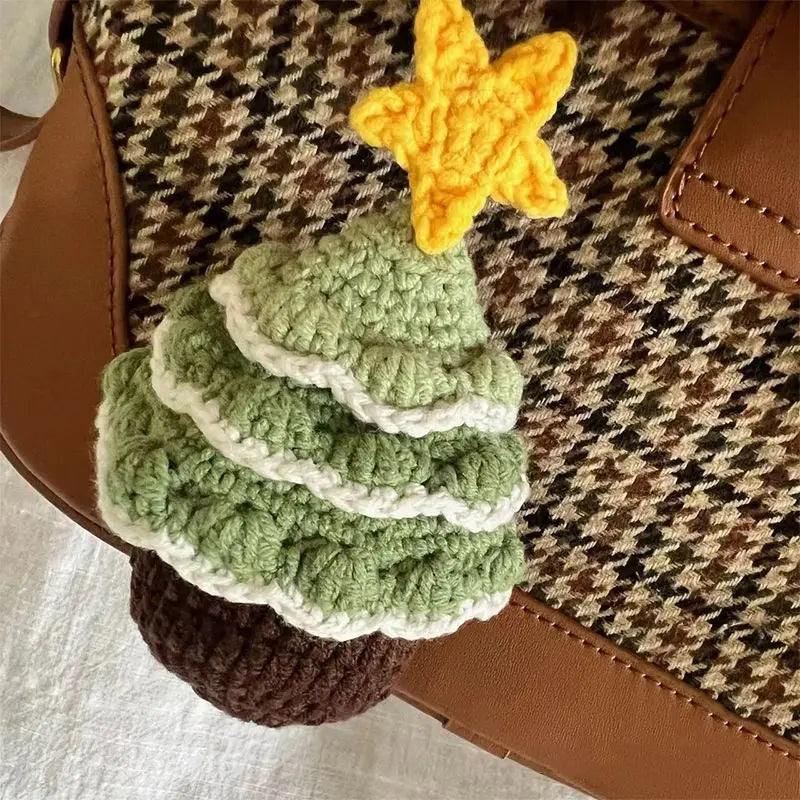 A crochet Christmas tree with a yellow star on top, made from green and white yarn, set against a brown and beige grid-patterned fabric.